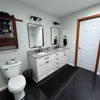 Modern bathroom with black floor, white vanity, two mirrors, toilet, and closed door