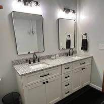 Bathroom vanity with two mirrors, dual sinks, white cabinets, and wall sconces above a granite countertop