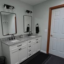 Bathroom vanity with double sinks, granite countertop, black mirrors, and a white door