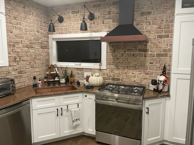 A kitchen with white cabinets, stainless steel appliances and a brick wall.