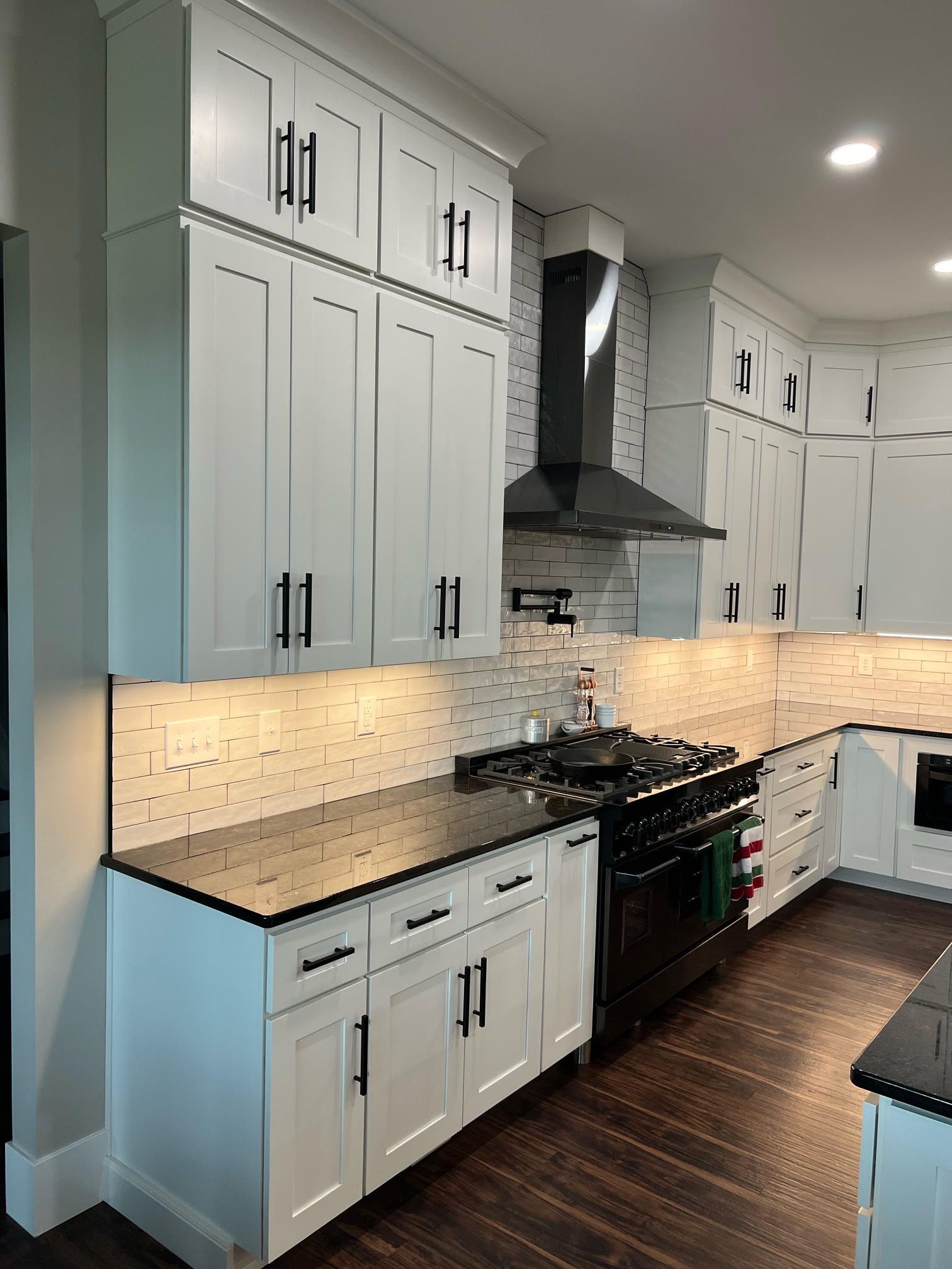 A kitchen with white cabinets, black countertop, a stove, and a hood