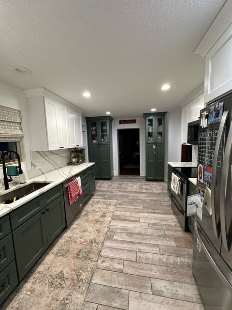 A kitchen with green cabinets, stainless steel appliances, a sink, and a refrigerator