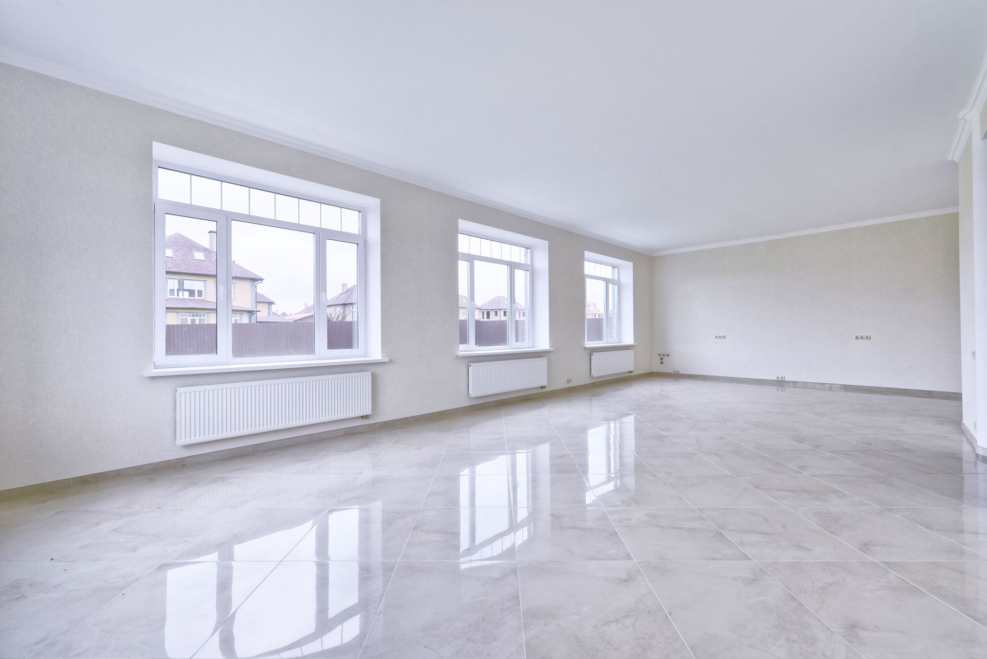 Empty room with three windows, white walls, and shiny tile floor.