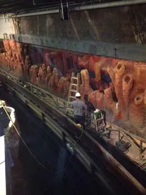 Workers on a ladder near an attraction's rock formations, possibly undergoing maintenance; dark setting.