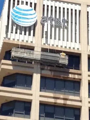 Workers on scaffolding cleaning windows of an AT&T building. The logo is visible.
