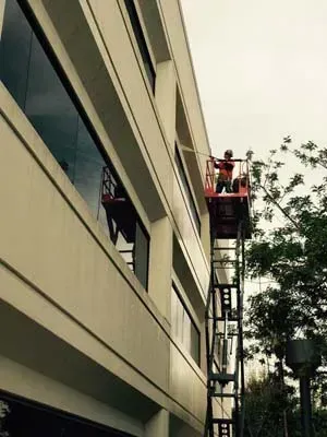 Person on a lift working on the exterior of a building. Beige walls, large windows. Cloudy day.