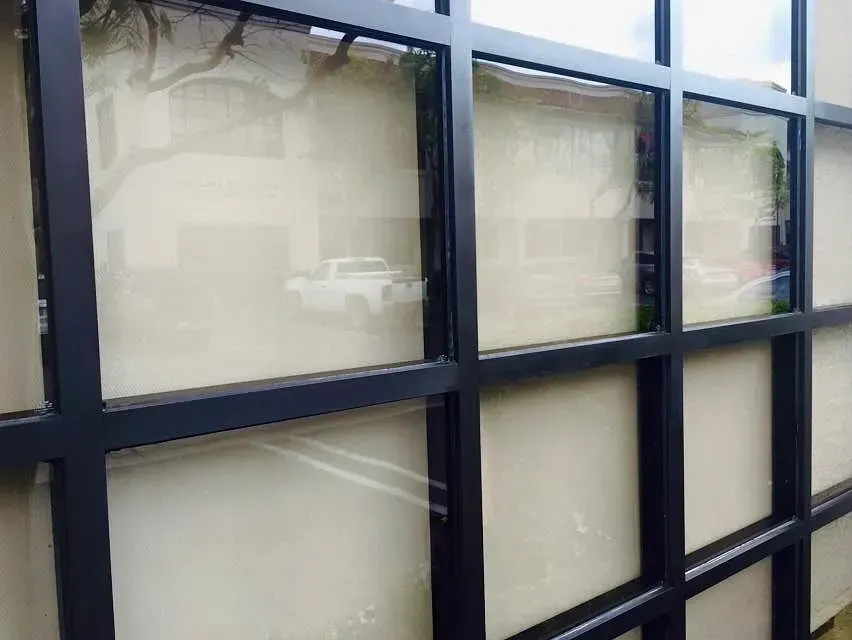 Black framed windows with light-colored interior, reflecting a blurred outdoor scene with a vehicle.