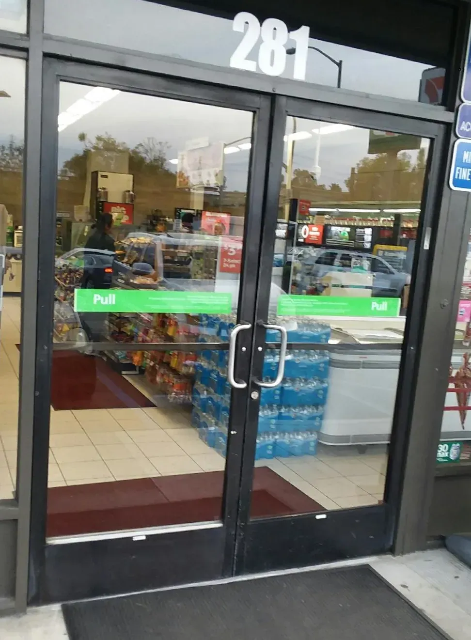 Exterior view of a convenience store with glass doors, showing a pull sign. Number 281 above the entrance.