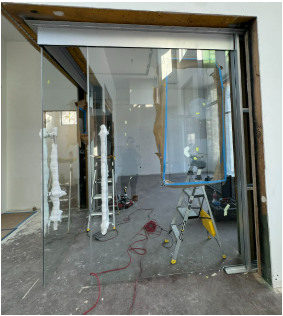 Glass storefront door in a construction zone with ladders, tools, and protective coverings.