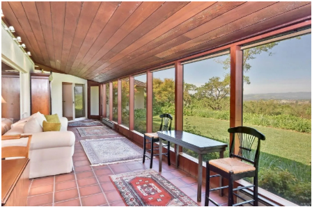 Sunroom with wood ceiling and large windows overlooking a green landscape. Two chairs sit at a table.