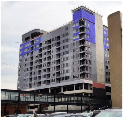 Construction of a tall gray and blue building. The structure is under construction with exposed elements.