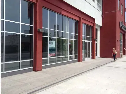 Exterior of a building with large windows and red accents; a person walks along the sidewalk.