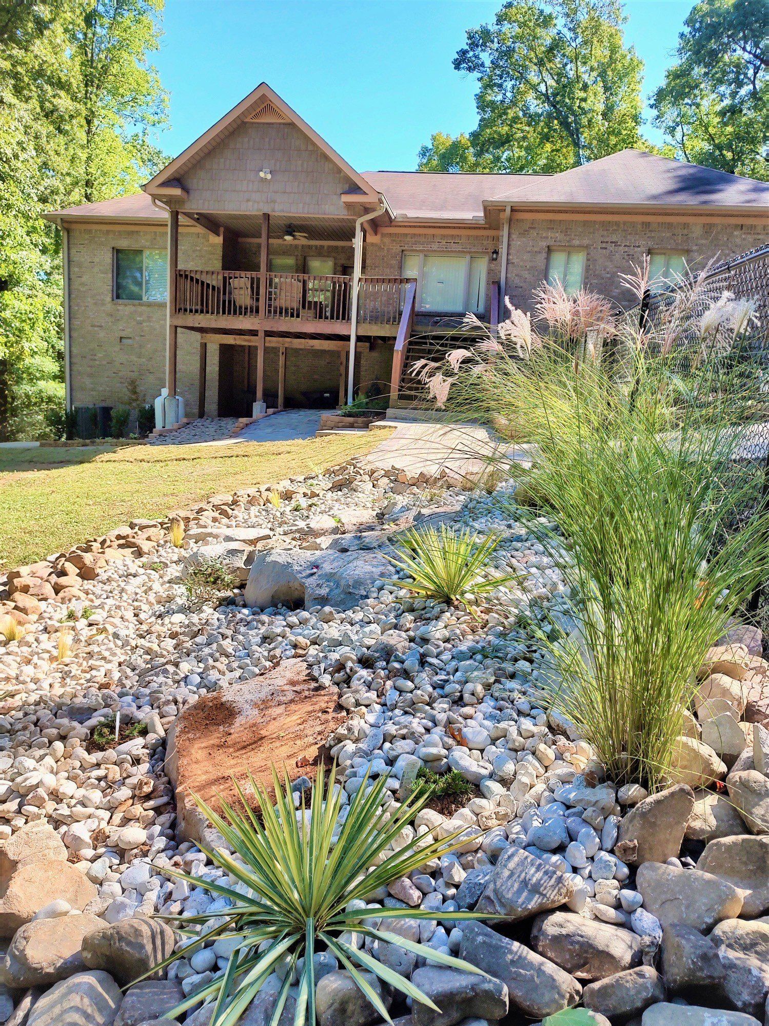 back yard of two story brick house with rock landscaping and plants after