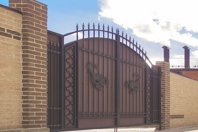 Tall black wrought-iron gate between brick walls under a blue sky