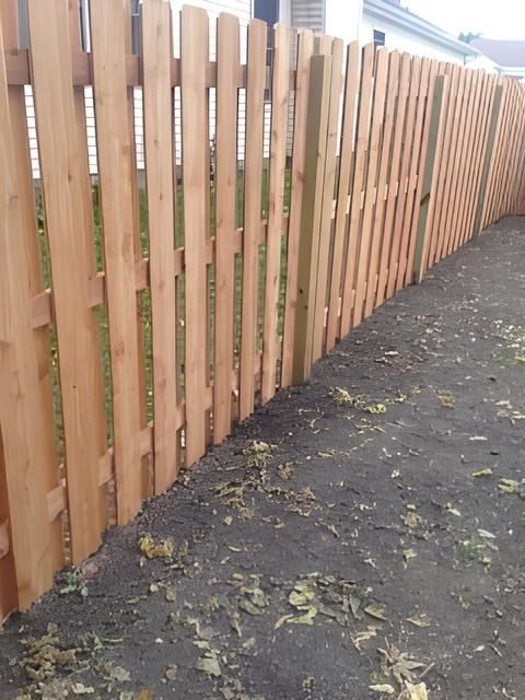 Wooden picket fence along a wet pavement beside a grassy area