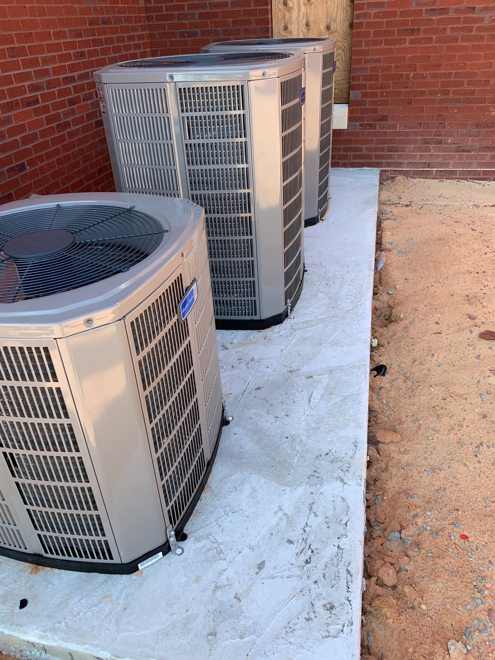 Three air conditioners are sitting on a concrete platform in front of a brick building.