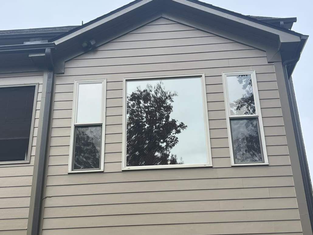 Tan house exterior with three windows reflecting a tree.