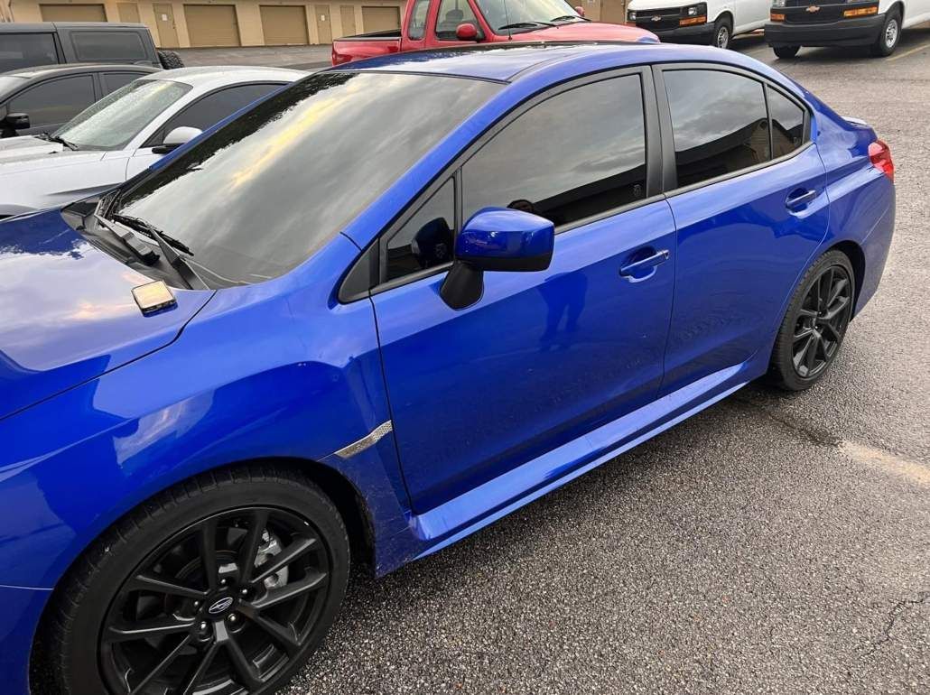 Blue Subaru WRX sedan with tinted windows, black wheels, parked in a lot.
