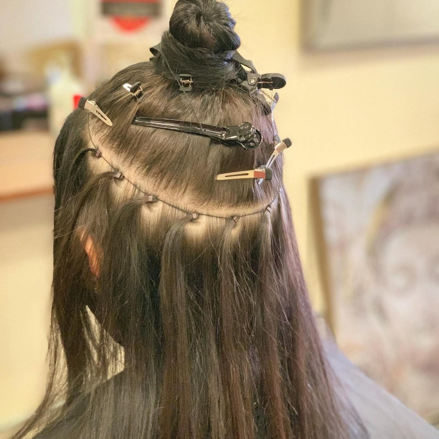 Hair extensions partially applied, held with clips. Dark hair with visible attachments, bun on top.