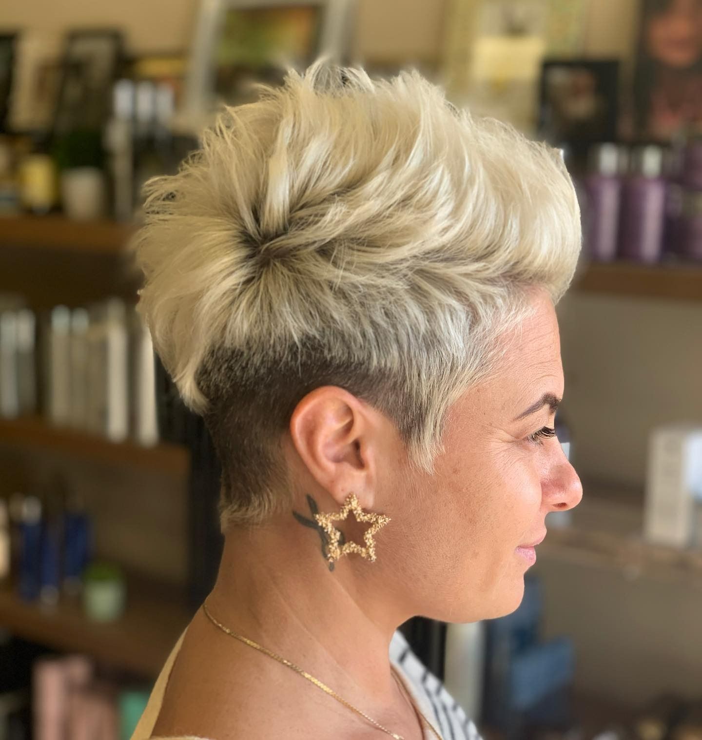 Woman with blonde, textured, short haircut, side profile; star earrings.