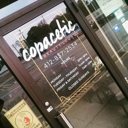 Copacetic Beauty Lounge storefront. White text on glass door shows hours, phone number, and name.