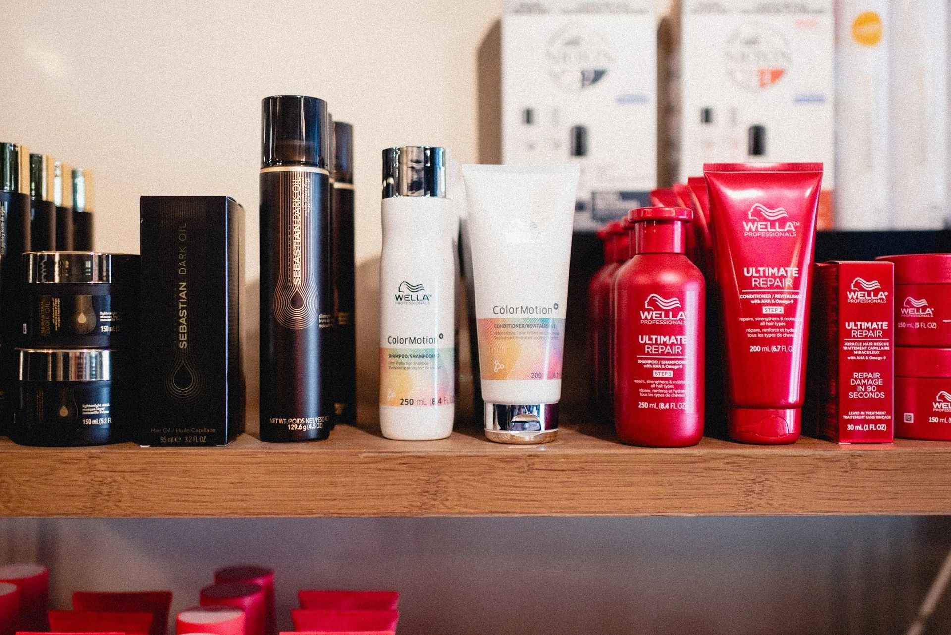 Hair care products arranged on a wooden shelf, featuring various brands and red and black packaging.