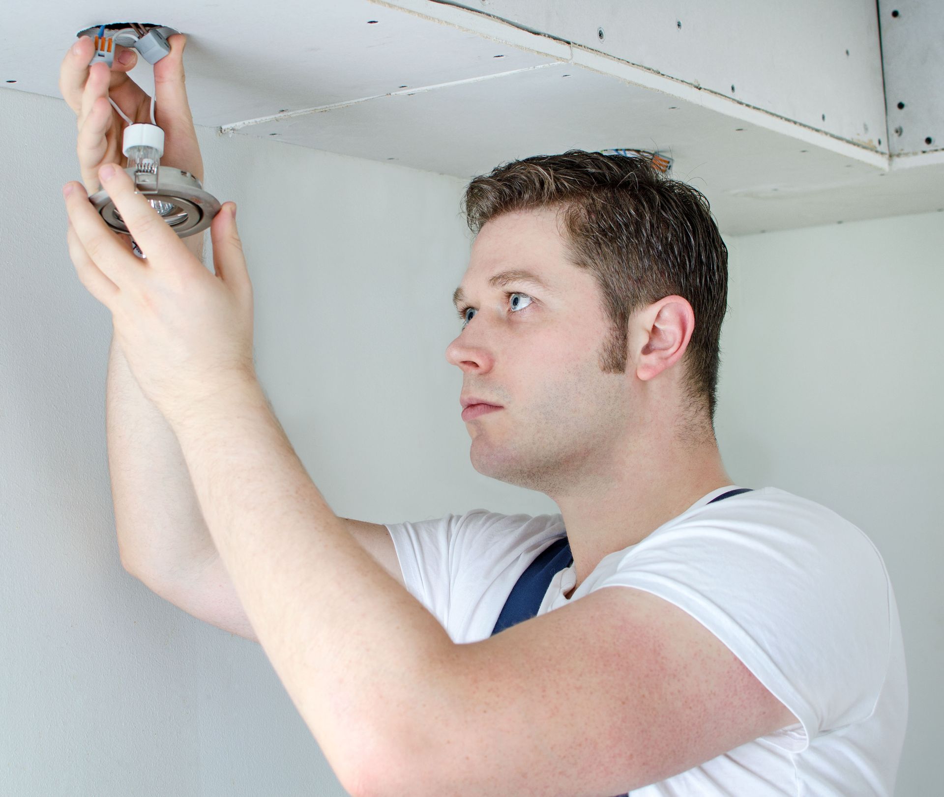 Man installing a light fixture in a white ceiling.