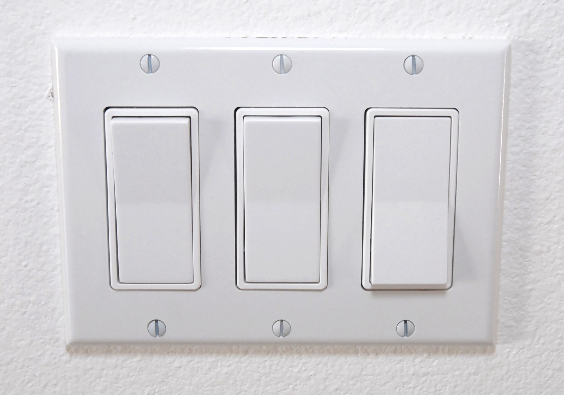 White triple-gang light switch plate with three rocker switches on a white wall.