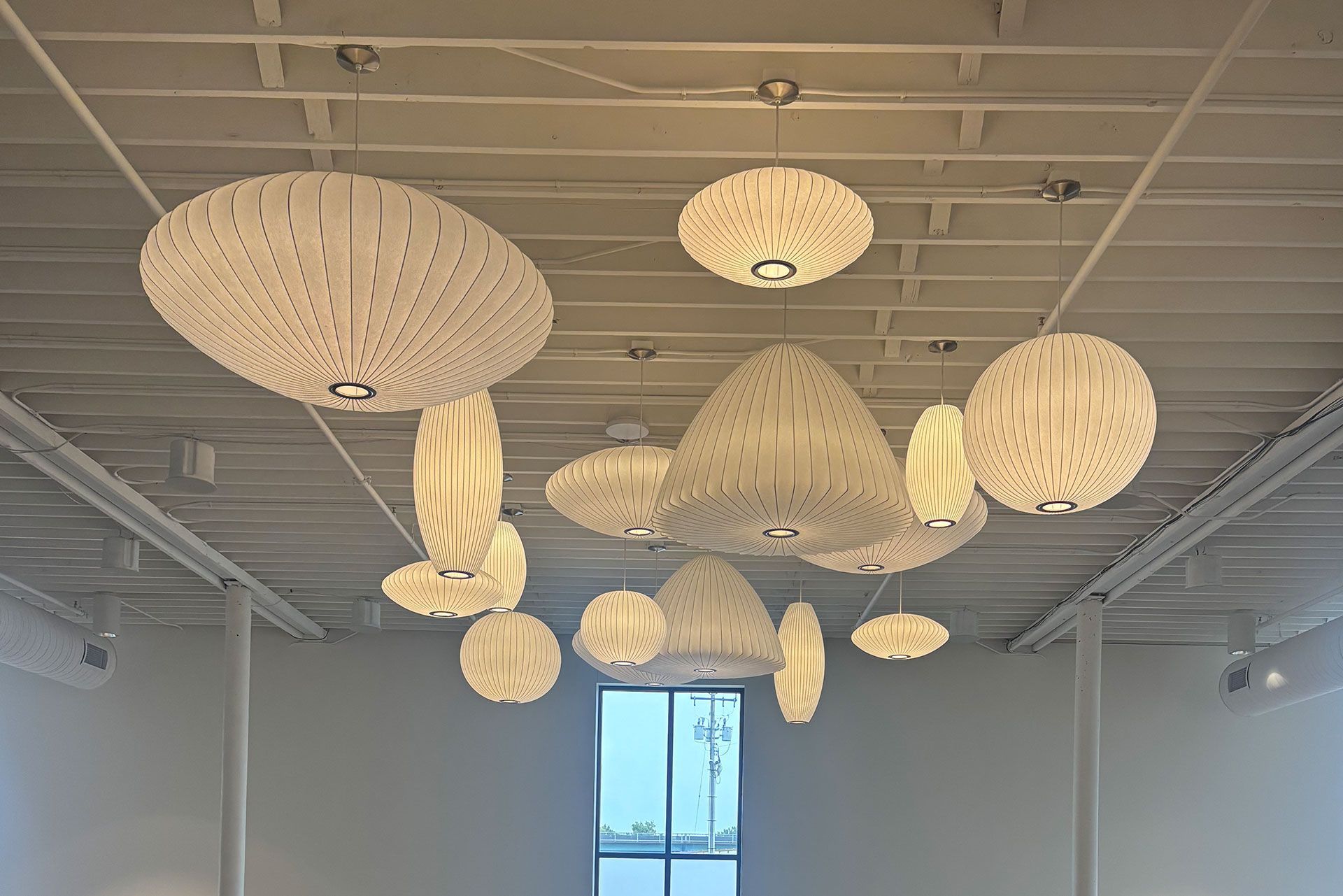 White pendant lights of various shapes hanging from a white ceiling.
