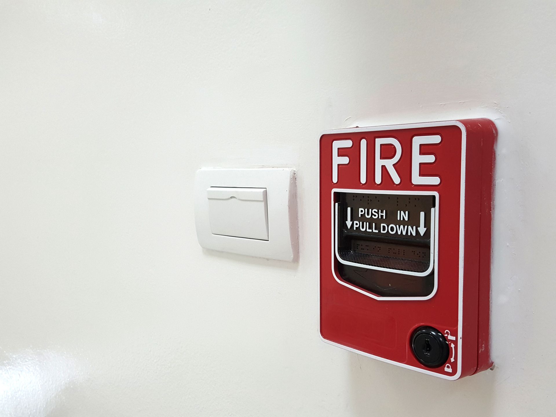 Red fire alarm box and white light switch on a white wall.