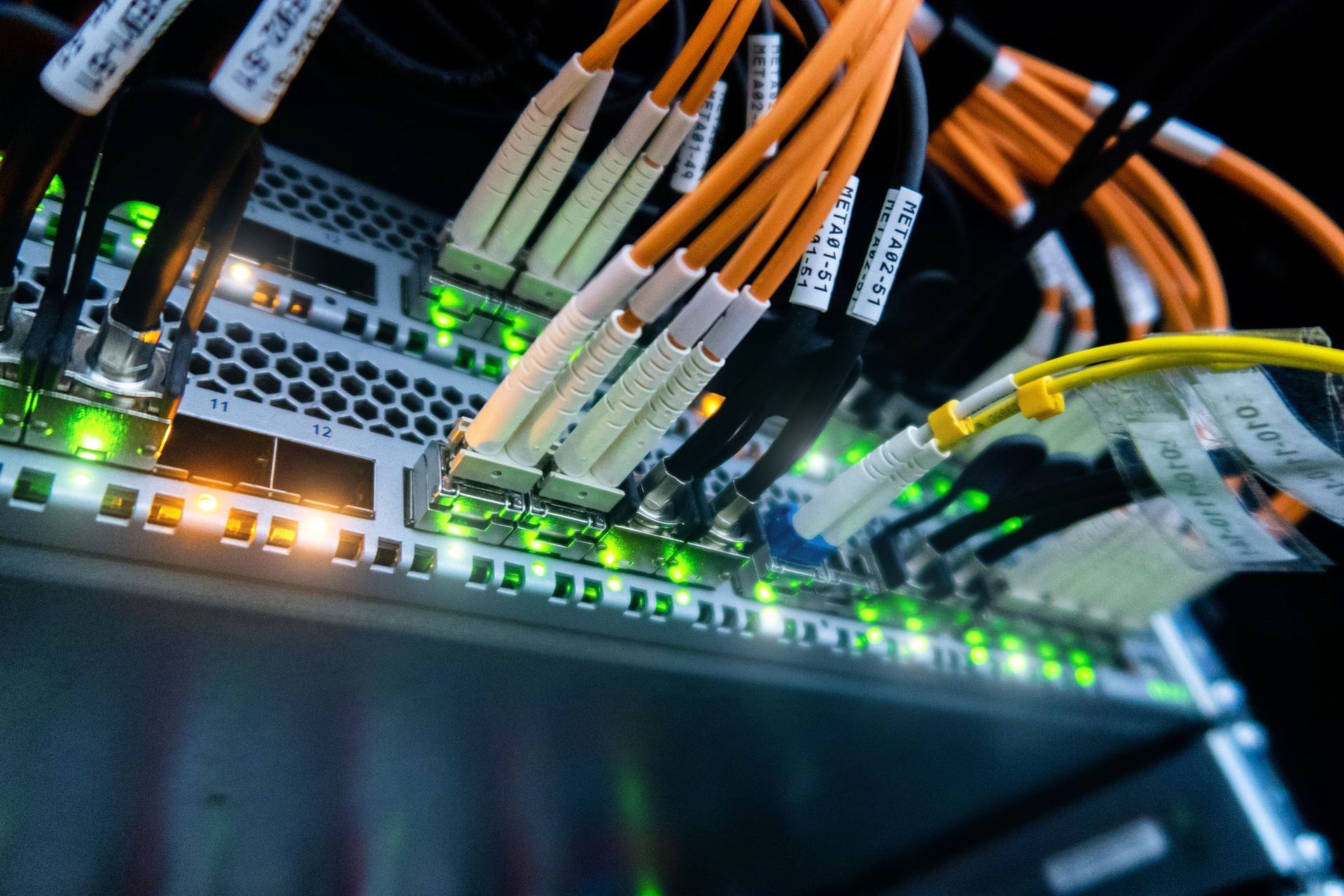 Server rack with orange and yellow fiber optic cables plugged in, green lights illuminated.
