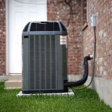 An air conditioner is sitting in the grass outside of a house 