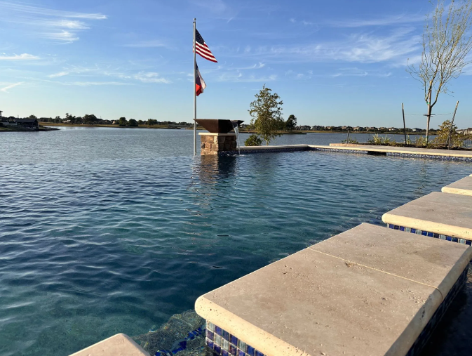 Infinity pool overlooking a lake, with American flag waving. Blue water, sunny sky.