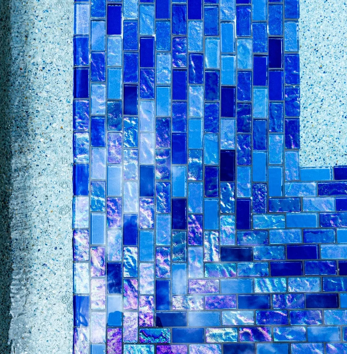 Blue mosaic tile wall inside a pool with light-colored concrete.