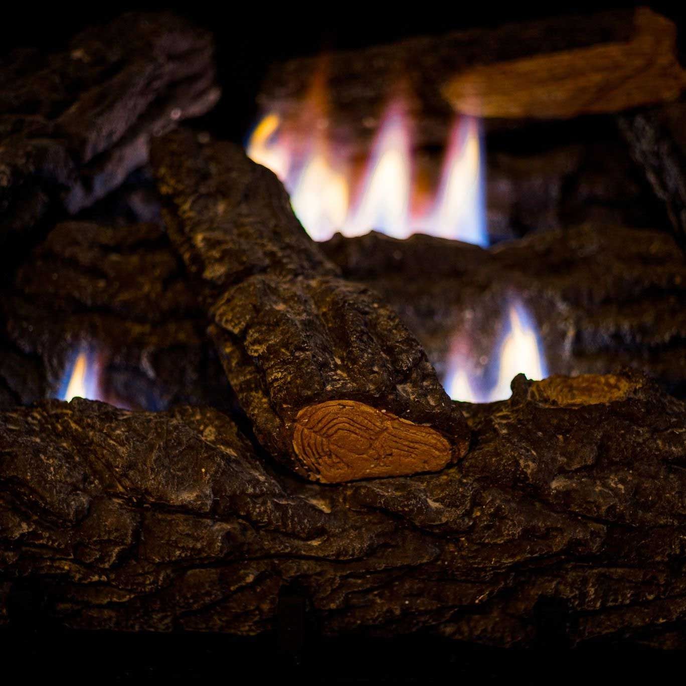 Fireplace with burning flames among dark, textured logs.