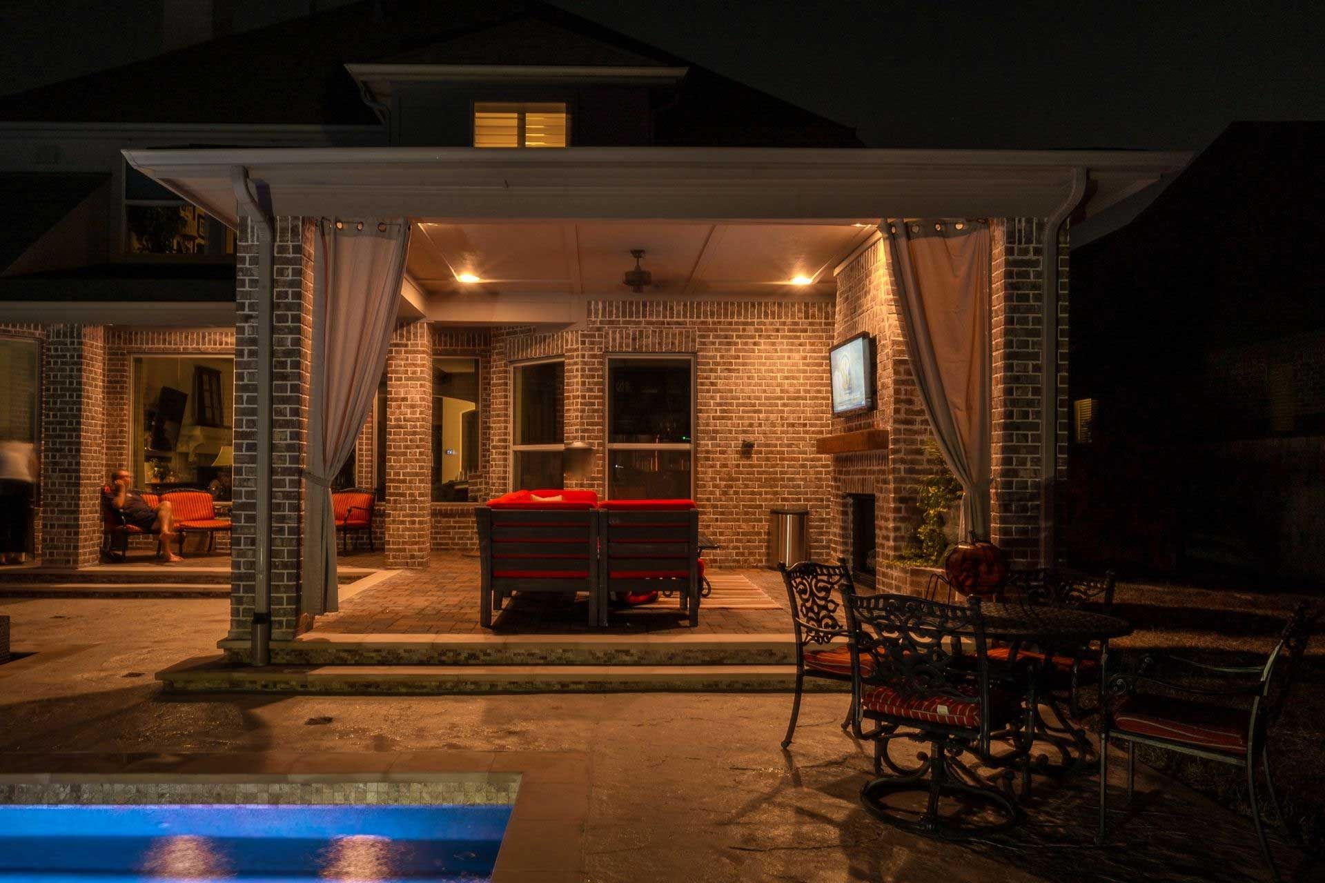 Outdoor patio lit at night, with a covered seating area near a pool.