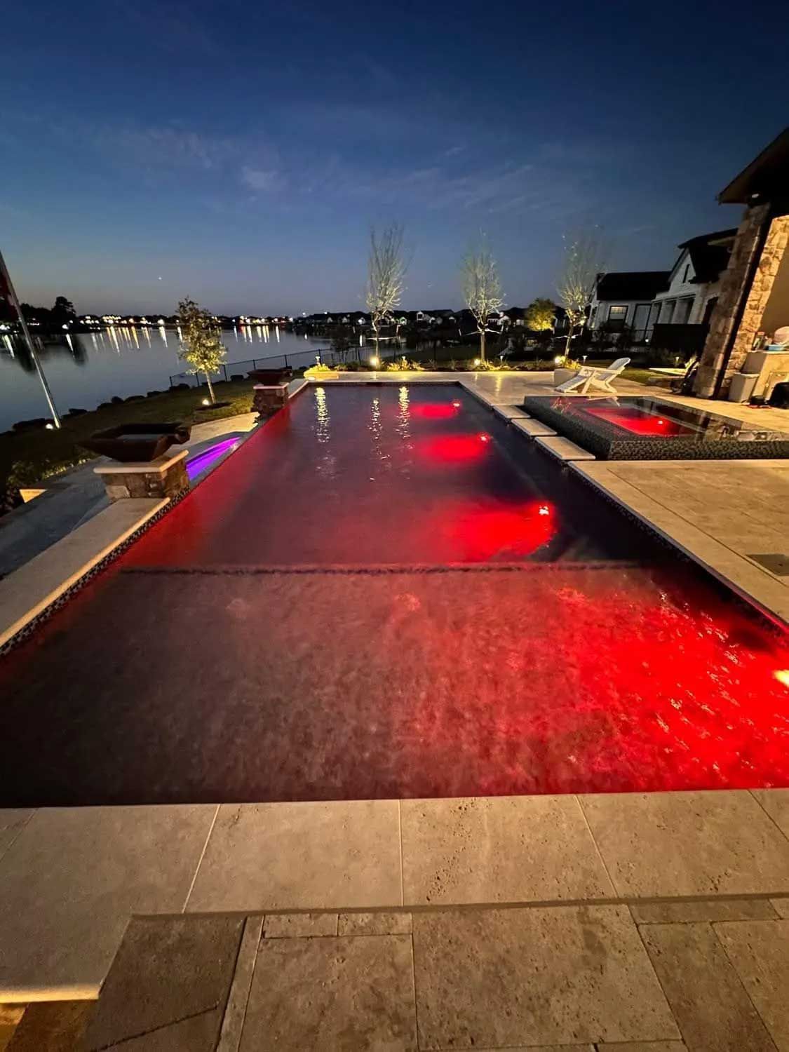 Night view of a long swimming pool with red lights, next to a lake.