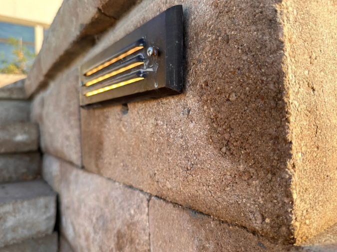 Black LED light fixture mounted on a textured brick wall, emitting warm yellow light.