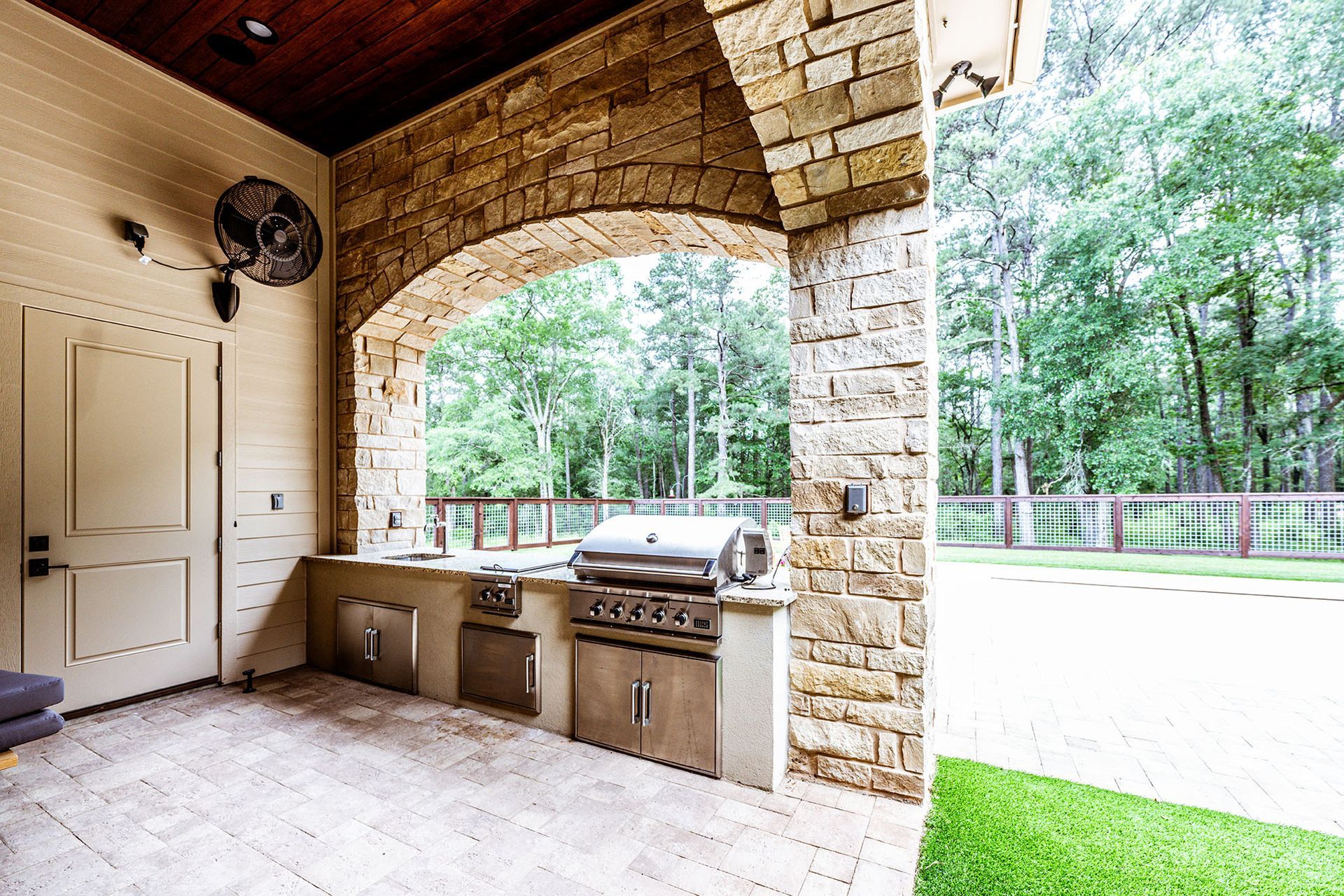 Outdoor kitchen with brick archway, grill, and stainless steel cabinets.