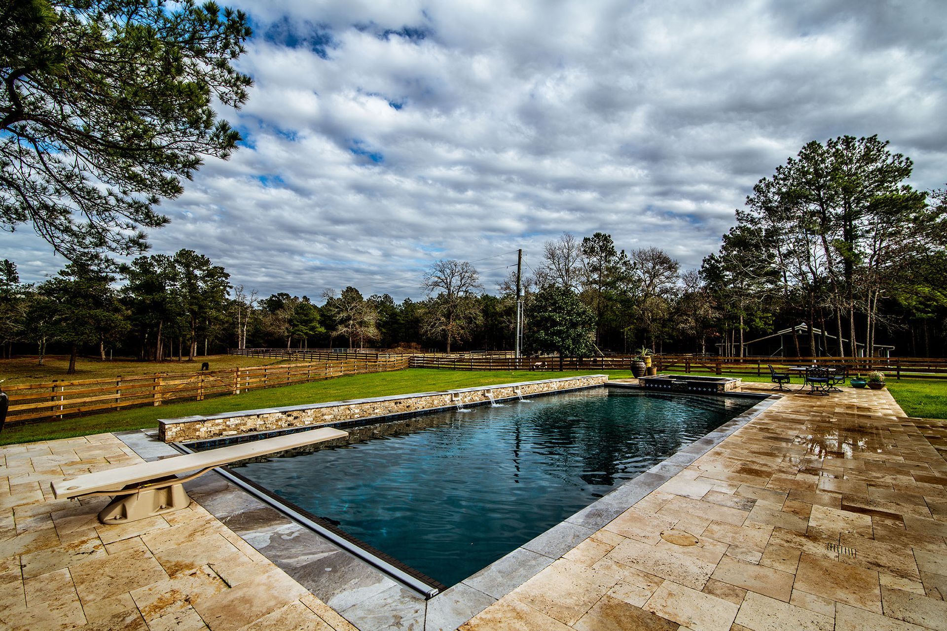 Swimming pool in a grassy backyard with trees under a cloudy sky.