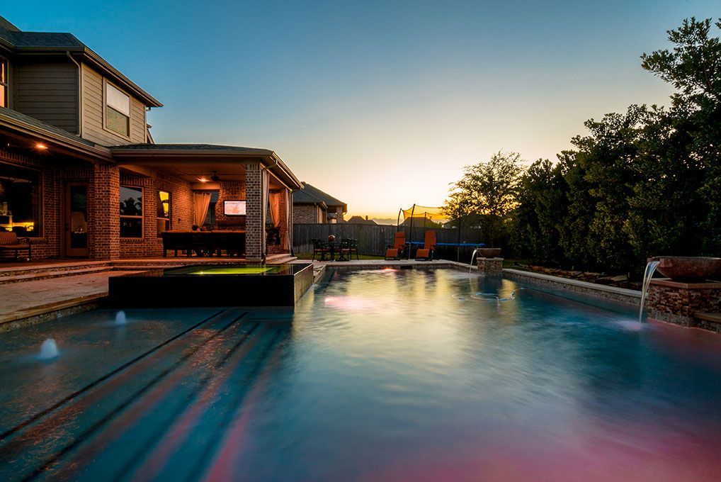 Pool at sunset with home in the background water features and outdoor living area.
