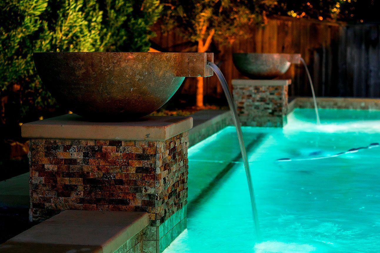 Water feature with lit pool at night two stone bowls pour water into the turquoise water.