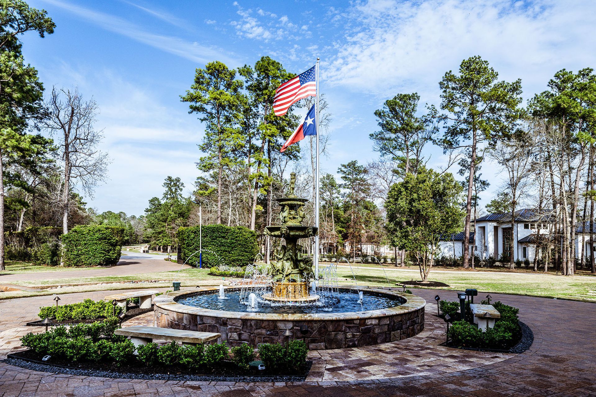 Fountain with water features, flags, and trees under a blue sky.