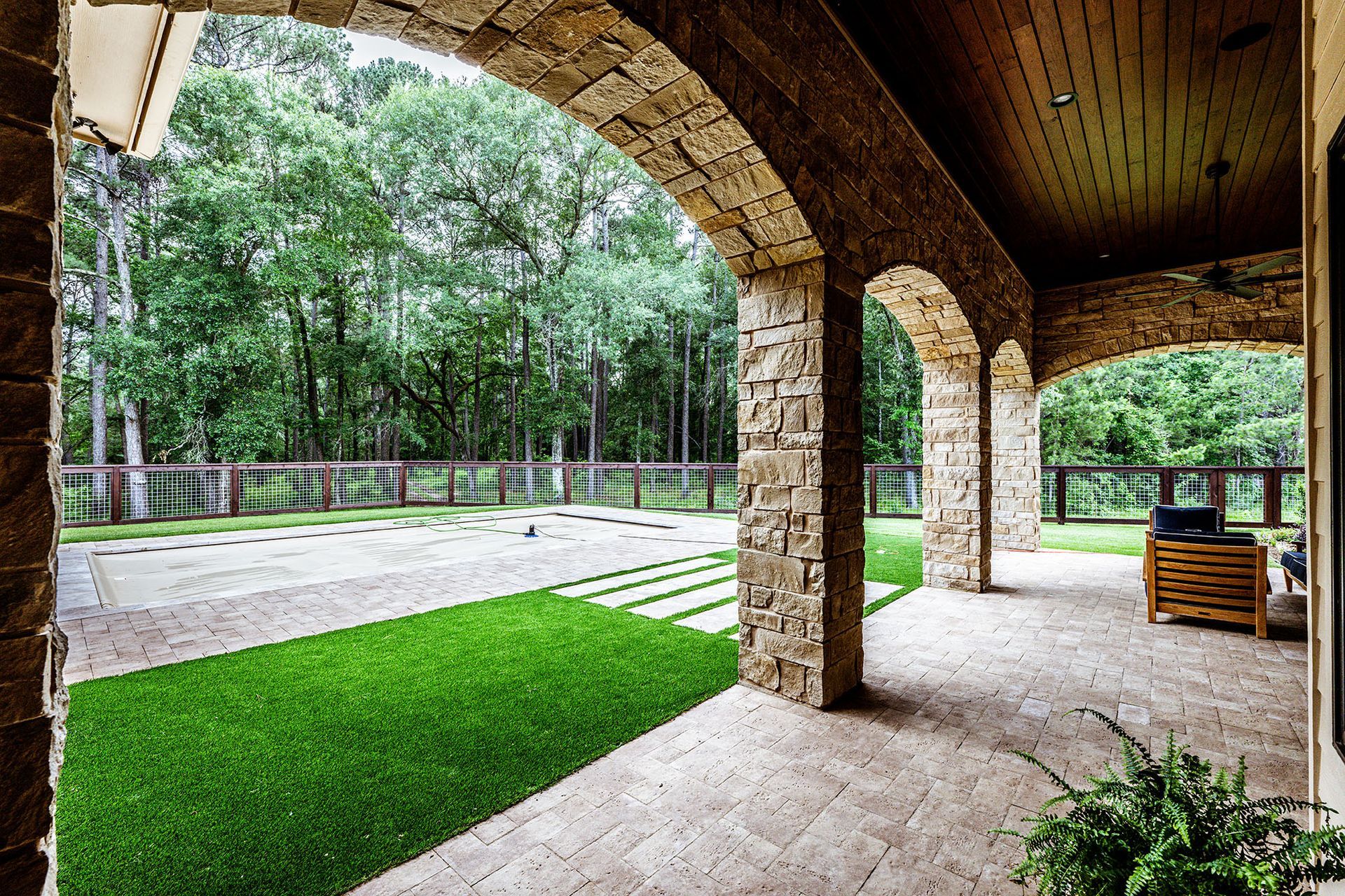 Stone arched veranda overlooking a lawn, paving, and a wooded area.