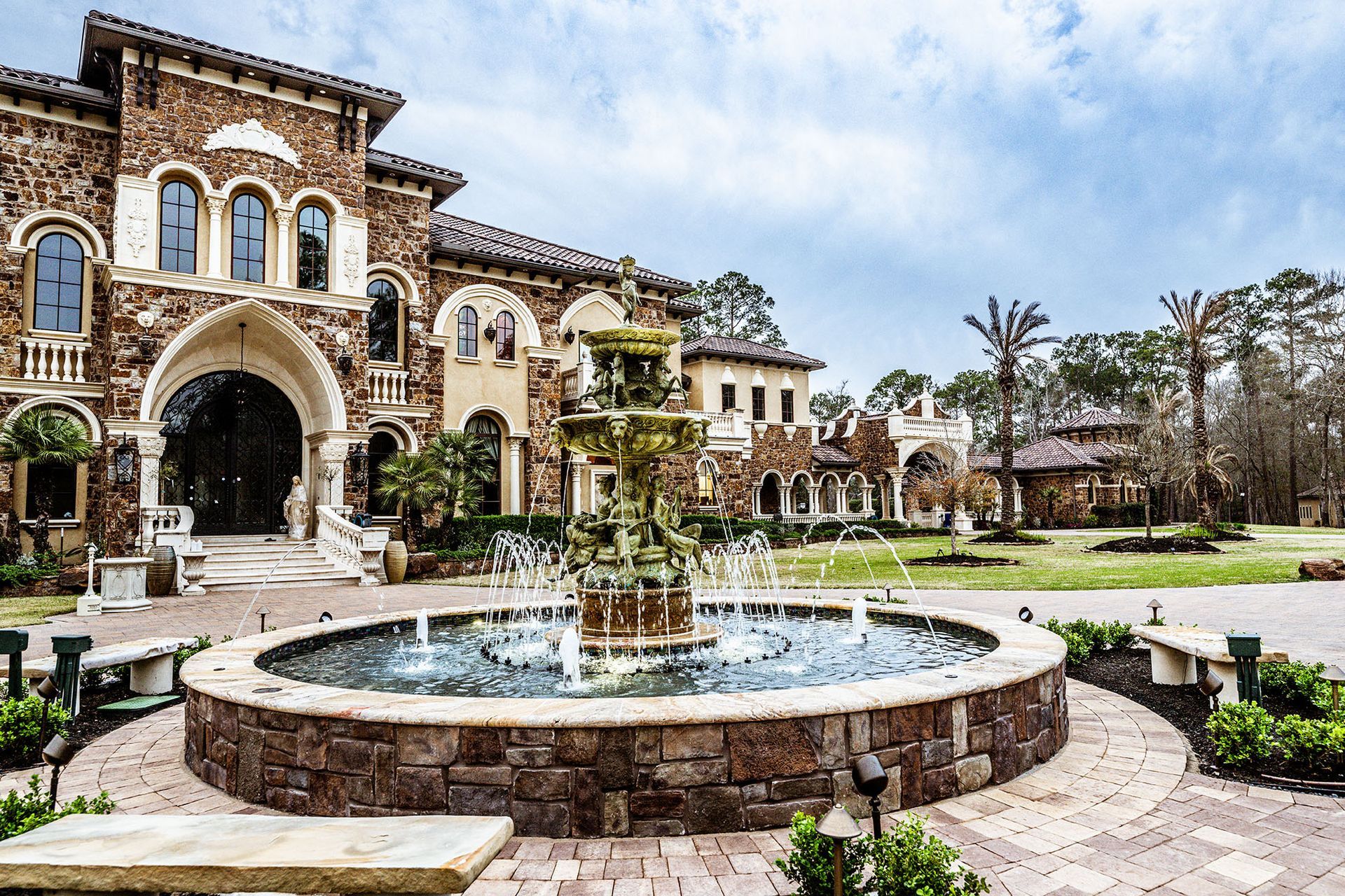 Ornate stone mansion with fountain and arched entrance.