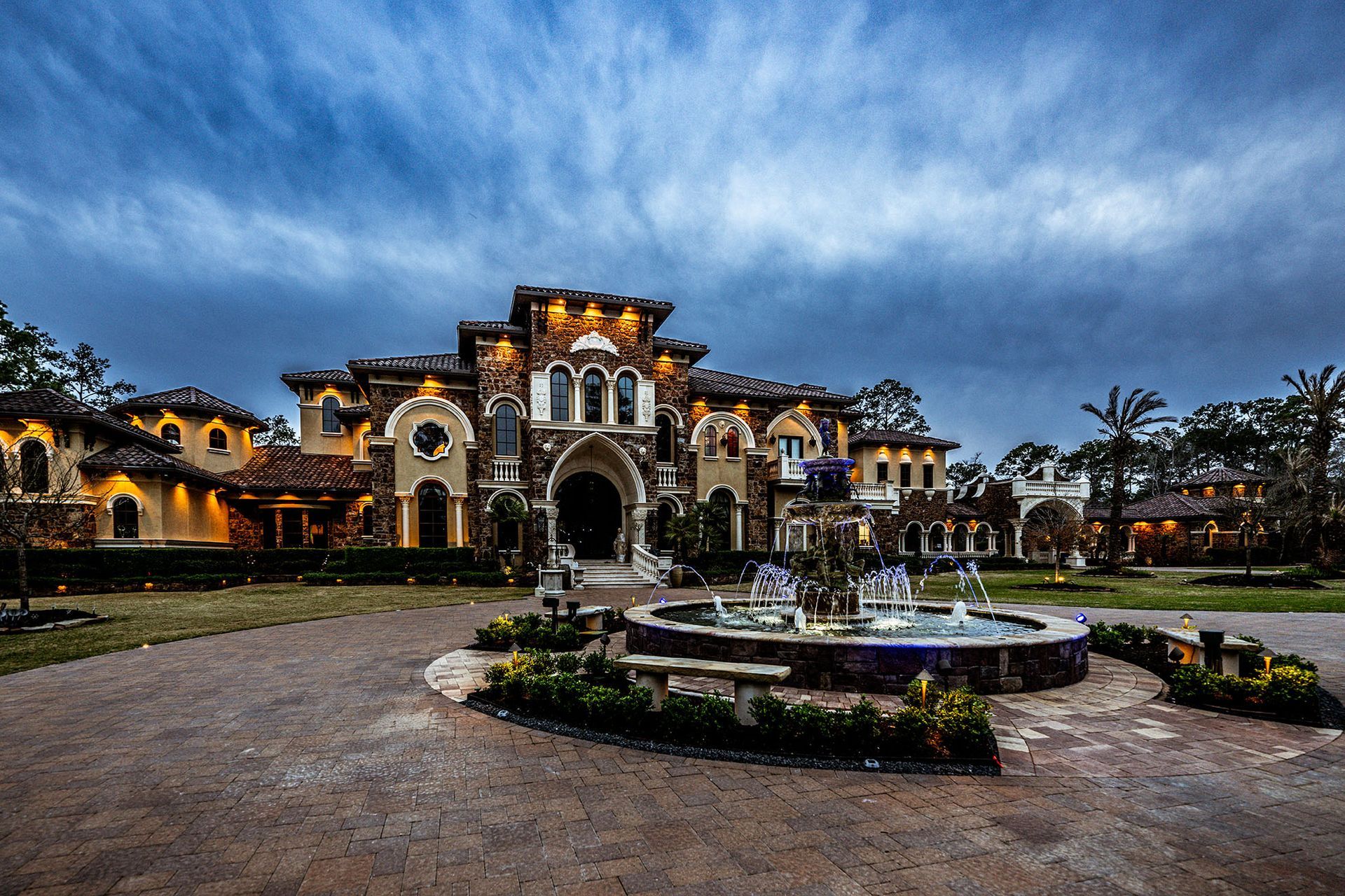 Large, ornate mansion with a fountain in front, against a cloudy sky.