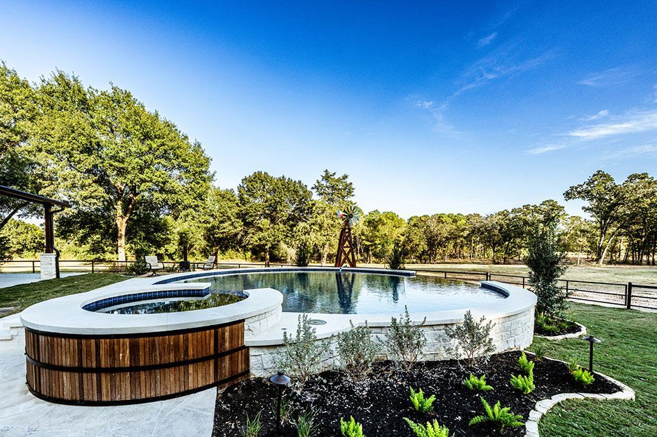 A pool and hot tub with a wooden surround, on a grassy lawn under a blue sky.