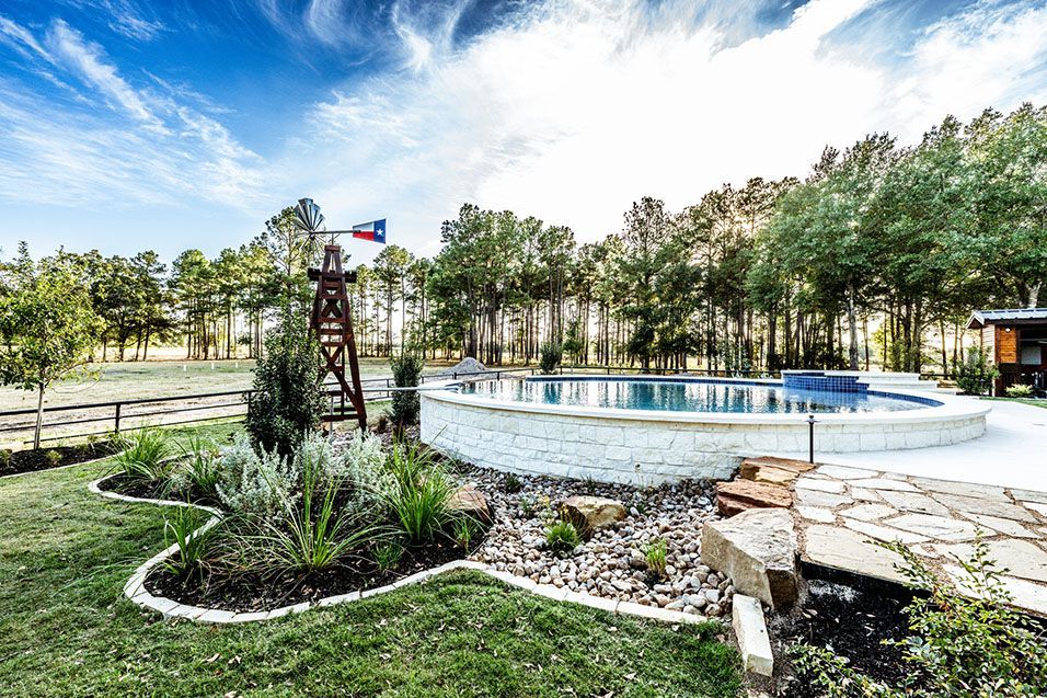 Pool and windmill in a backyard, with lush landscaping and blue sky.