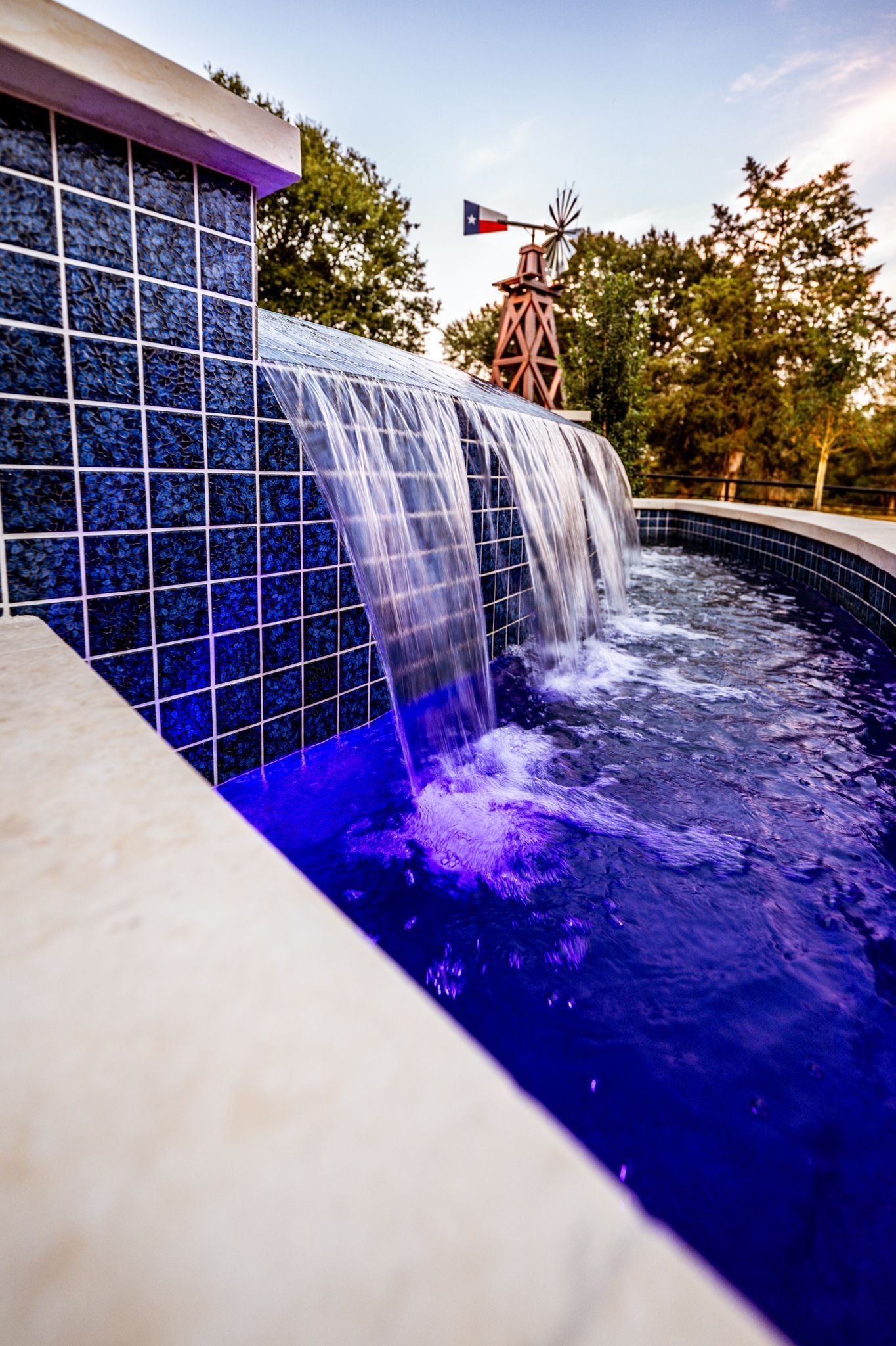 Waterfall feature cascading into a pool with blue mosaic tiles, windmill in the background.