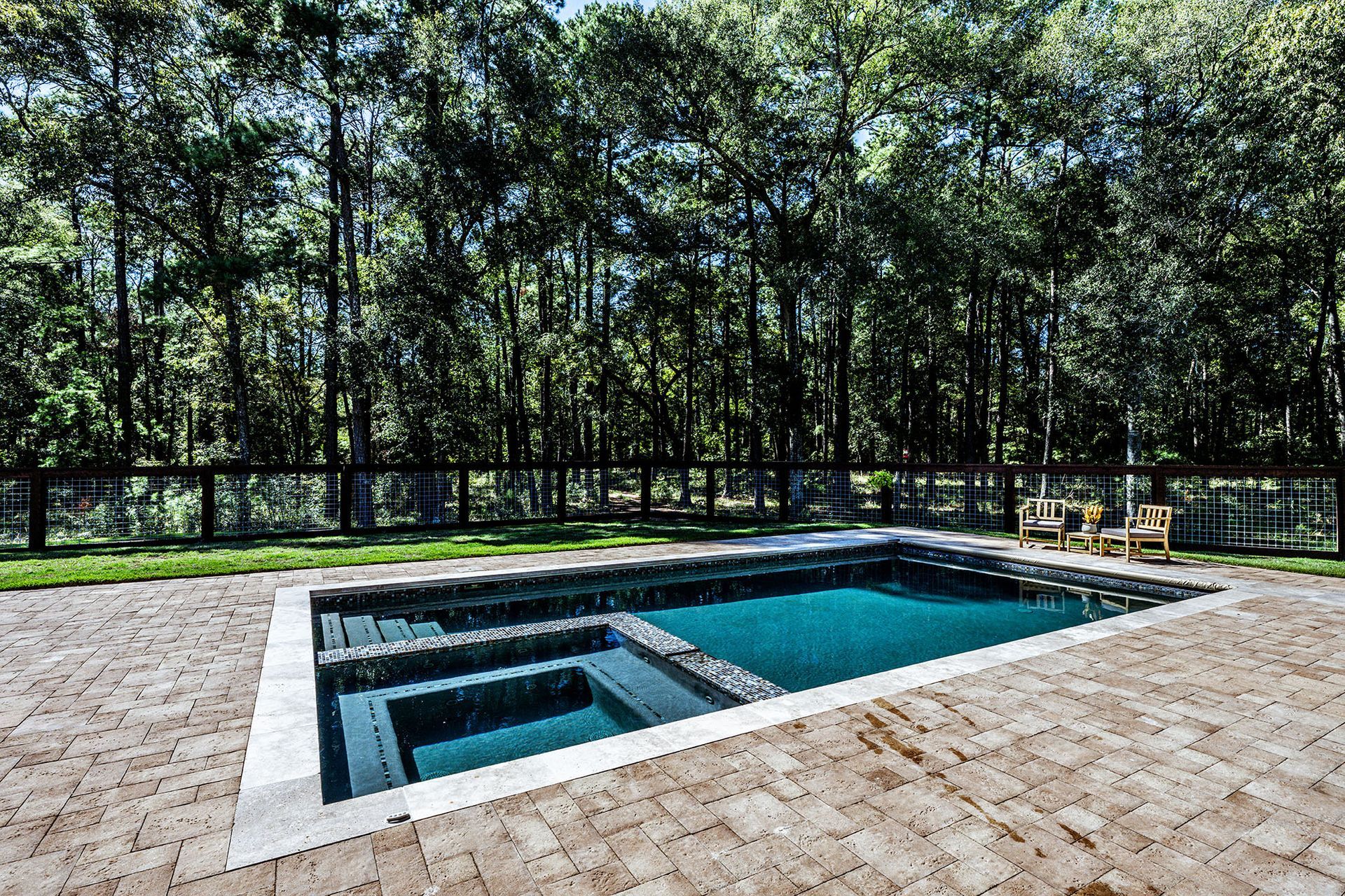Backyard pool with stone patio, surrounded by trees.